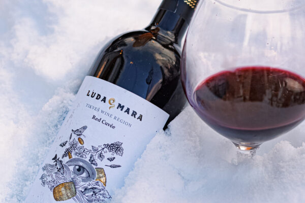 A bottle of Luda Mara red wine from the Tikveš region resting in the snow beside a partially filled wine glass.