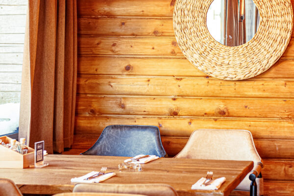 A cozy, wood-paneled dining area with leather chairs around a wooden table, a woven circular mirror on the wall, and straw-like lighting overhead.