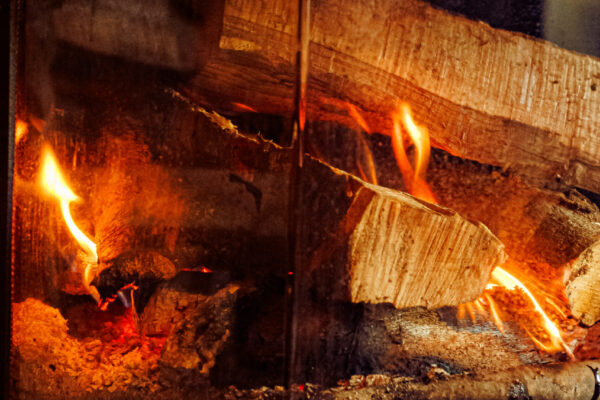 A close-up of stacked wooden logs burning inside a glass-enclosed fireplace.