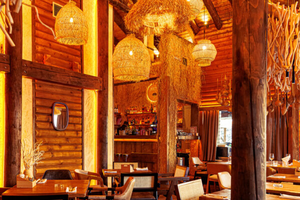 A spacious, wood-beamed restaurant interior adorned with straw and twig chandeliers, warm lighting, and wooden tables arranged throughout.
