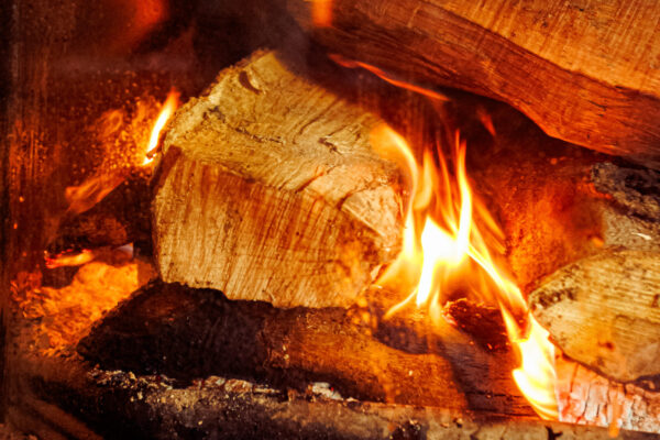 A close-up of wooden logs aflame inside a glass-enclosed fireplace, with glowing embers and flickering flames.