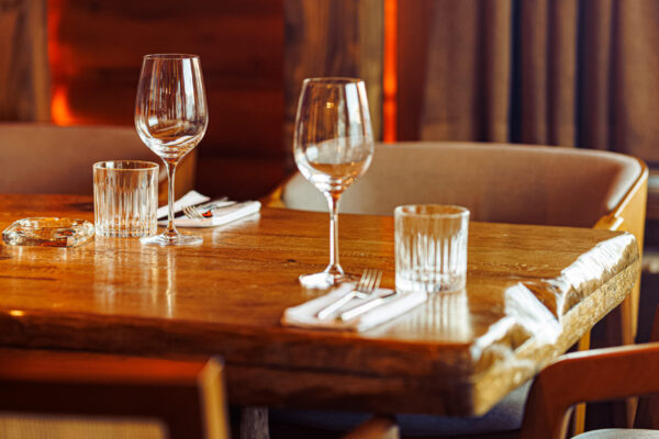 A wooden table set with wine glasses and water glasses in a warmly lit, rustic dining area.