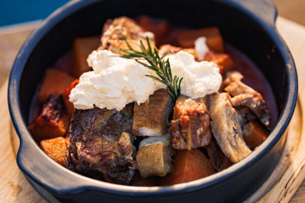 A black ceramic dish filled with chunks of meat, root vegetables,