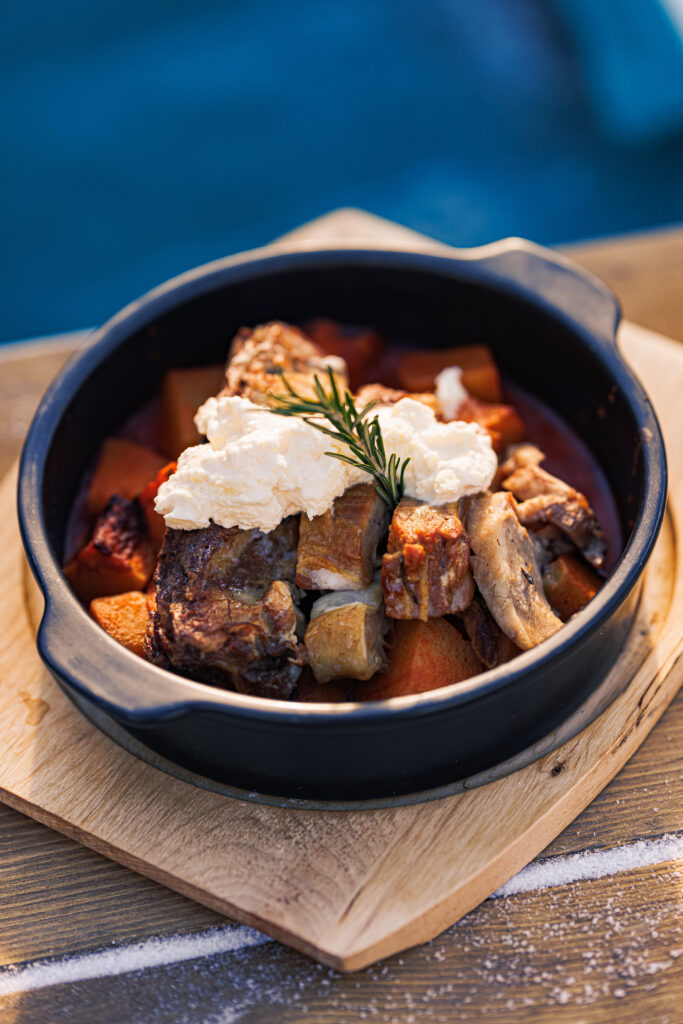 A black ceramic dish filled with chunks of meat, root vegetables,